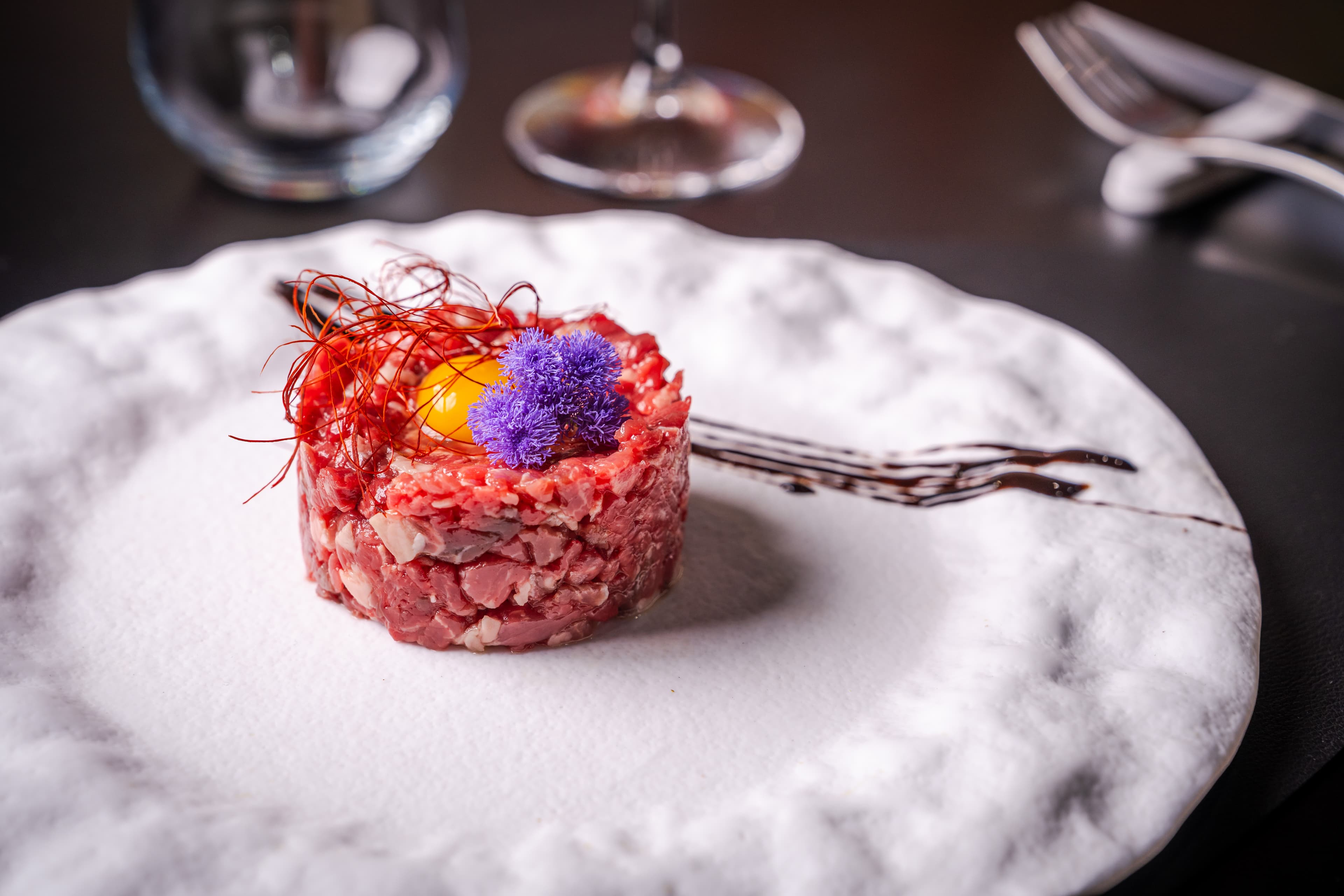 Battuta di manzo servita su piatto materico con tuorlo e fiori